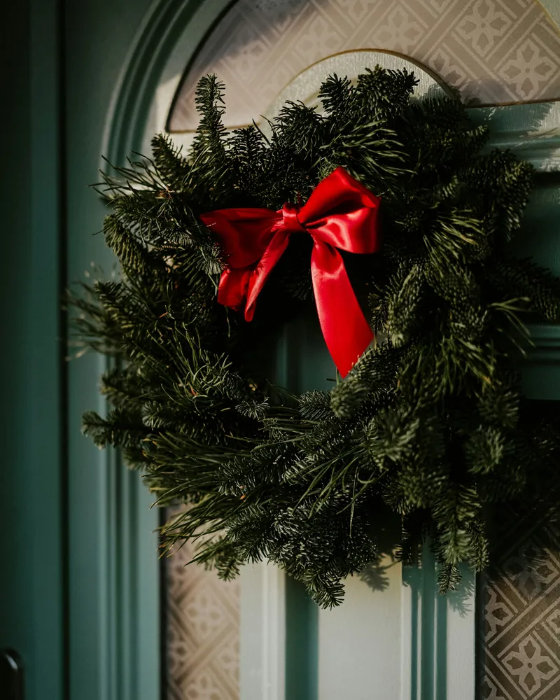 Guirlanda de pinheiro com laço de cetim vermelho em uma porta verde de entrada com parede decorada