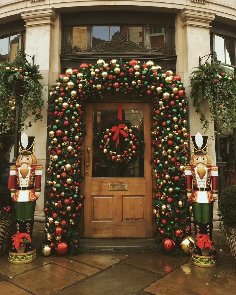 Entrada ampla emoldurada por um grande arco de bolas vermelhas, verdes e douradas, com guirlanda na porta e soldadinhos quebra-nozes dos dois lados